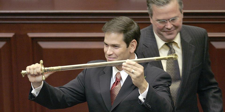Marco Rubio holds a sword in front of Jeb Bush