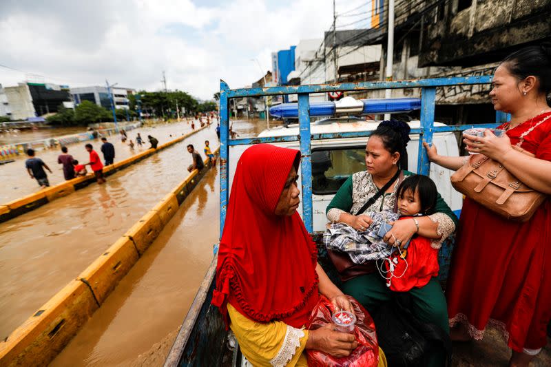 Locals ride on the back of a truck to travel across a flood-affected area after heavy rains in Jakarta