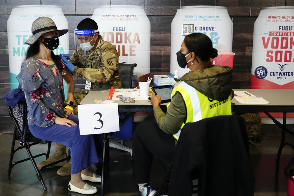 FILE - In this March 25, 2021, file photo, Jing Wang, left, receives a vaccine at Mercedes-Benz Stadium in Atlanta. A new poll from The Associated Press-NORC Center for Public Affairs Research shows that the percentage of Americans resisting getting inoculated has shrunk in the past few months. But it’s still not enough to pull America out of the pandemic, and reach herd immunity. (AP Photo/Brynn Anderson, File)