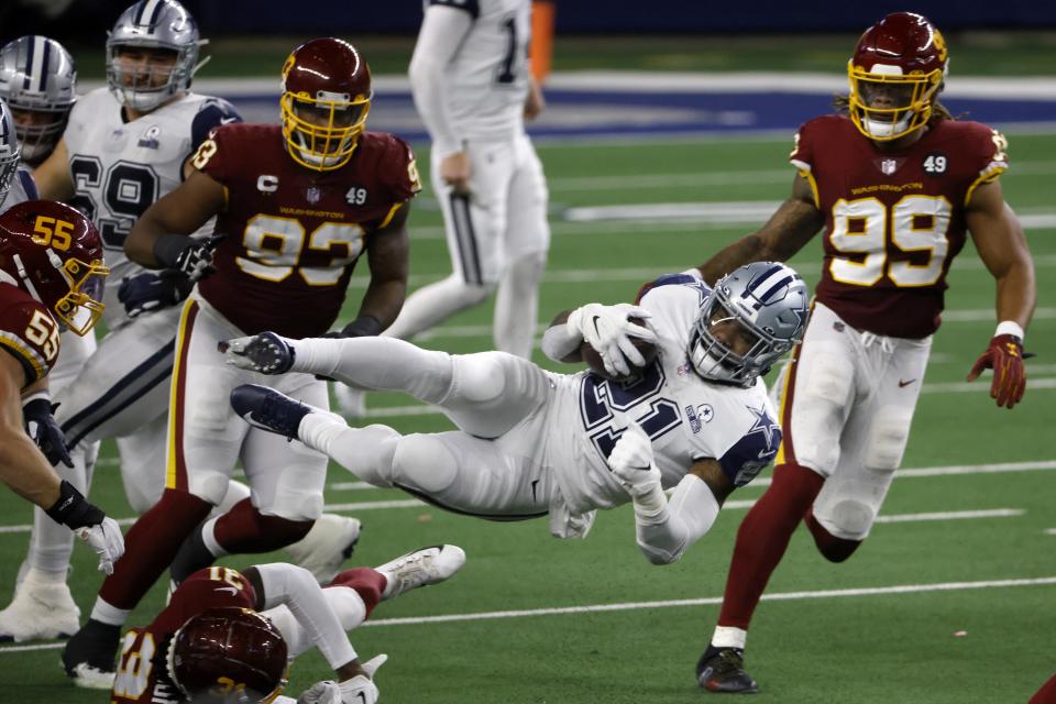 Dallas Cowboys running back Ezekiel Elliott (21) leaps forward on a carry for a first down between Washington Football Team's Cole Holcomb (55), Kamren Curl (31), Jonathan Allen (93) and Chase Young (99) in the second half of an NFL football game in Arlington, Texas, Thursday, Nov. 26, 2020. (AP Photo/Ron Jenkins)