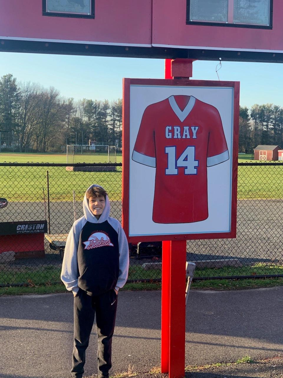 Thomas Gray stands next to the mounted jersey of his uncle Chris Gray at Manalapan High School's football field.