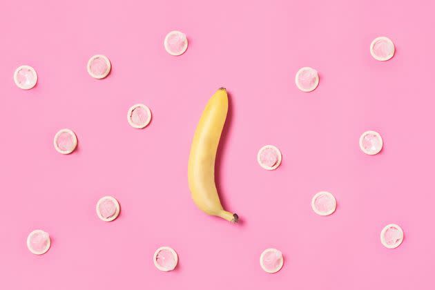 A yellow banana on a pink background surrounded by latex condoms in a random pattern. Concept to illustrate safe sex and male contraception. Shot with a with a top down view