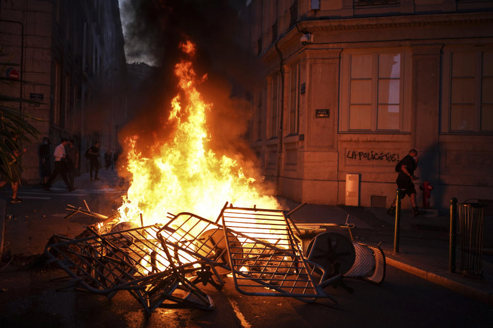 A man passes by a wall illuminated by a burning barricade on which is written 'Police kills' in the center of Lyon, central France, Friday, June 30, 2023. French President Emmanuel Macron urged parents Friday to keep teenagers at home and proposed restrictions on social media to quell rioting spreading across France over the fatal police shooting of a 17-year-old driver. Writing on wall reads in French "Justice for Nahel" (AP Photo/Laurent Cipriani)