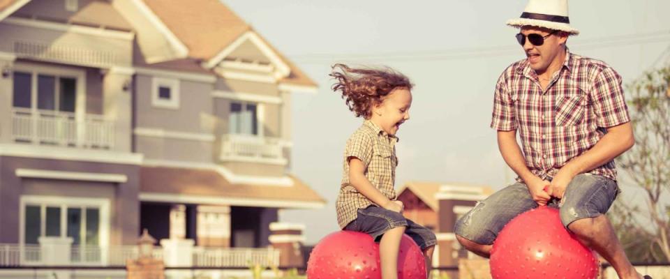 Dad and son jumping on inflatable balls on the lawn in front of house at the day time