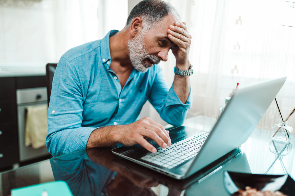 Tired and exhausted mature man working from home and using laptop