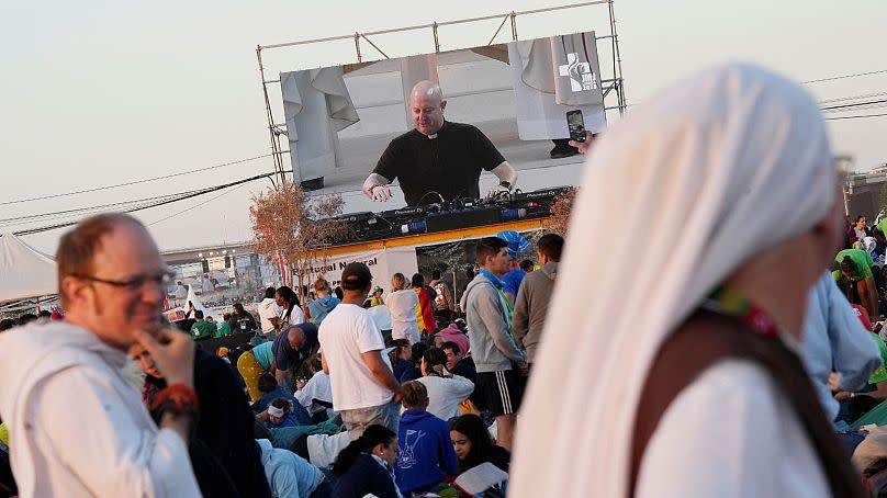 Guilherme Peixoto, on video screen, plays techno music to help pilgrims wake up at Parque Tejo in Lisbon - August 2023