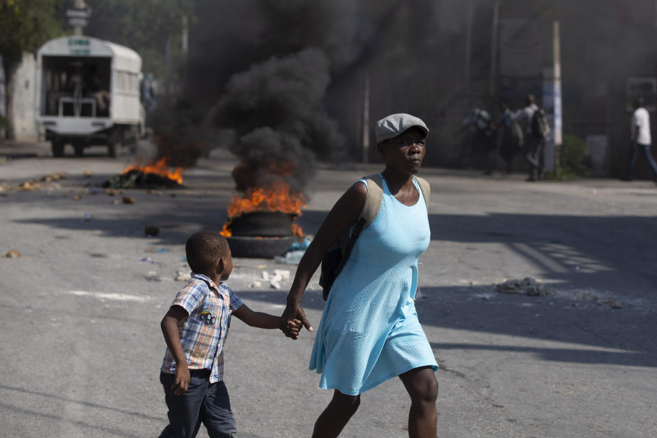 A child, walking hand-in-hand with his mother, looks over at a burning barricade set up by friends and relatives of James Philistin who was kidnapped last night, in Port-au-Prince, Haiti, Wednesday, Nov. 24, 2021. (AP Photo/Odelyn Joseph)