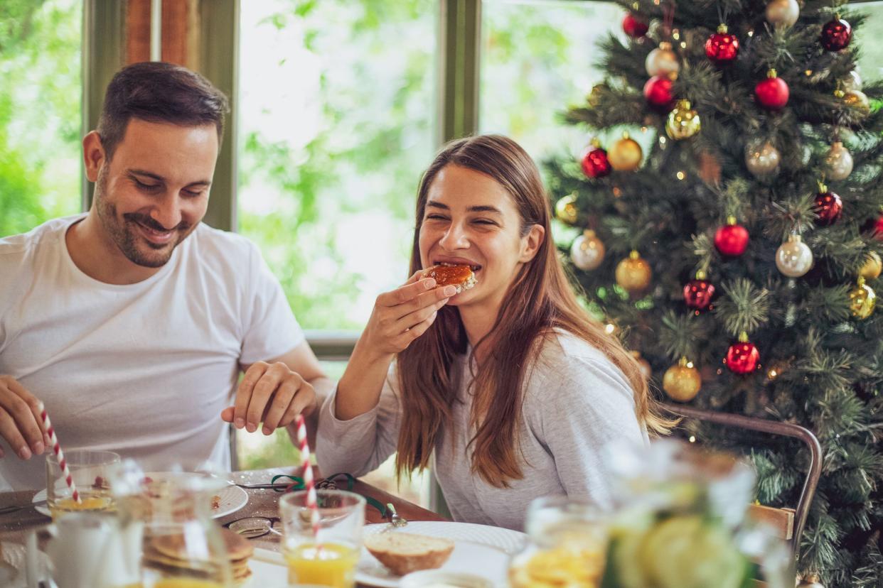 A handsome young couple having breakfast on Christmas morning. A beautifully decorated pine tree is in the background