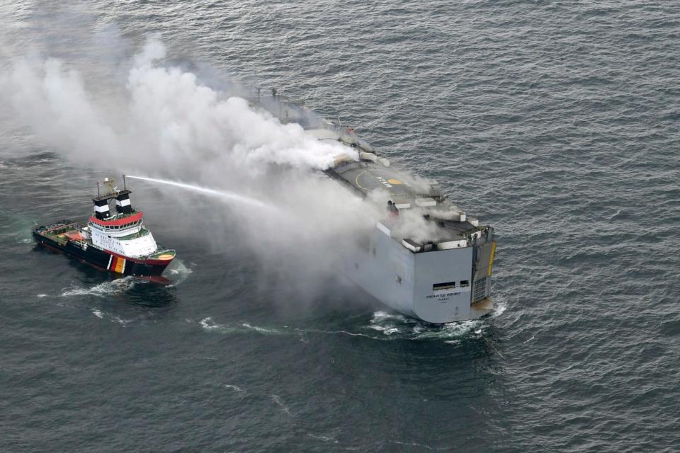 A boat hoses the smoke from a fire which broke out on a freight ship in the North Sea, about 27 kilometers (17 miles) north of the Dutch island of Ameland, Wednesday, July 26, 2023. A fire on the freight ship Fremantle Highway, carrying nearly 3,000 cars, was burning out of control Wednesday in the North Sea, and the Dutch coast guard said it was working to save the vessel from sinking close to an important habitat for migratory birds. (Kustwacht Nederland/Coast Guard Netherlands via AP)