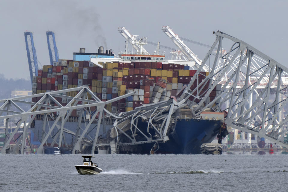 A boat moves past a container ship as it rests against wreckage of the Francis Scott Key Bridge on Tuesday, March 26, 2024, as seen from Pasadena, Md. The container ship lost power and rammed into the major bridge in Baltimore early Tuesday, causing it to snap and plunge into the river below. Several vehicles fell into the chilly waters, and rescuers searched for survivors. (AP Photo/Mark Schiefelbein)