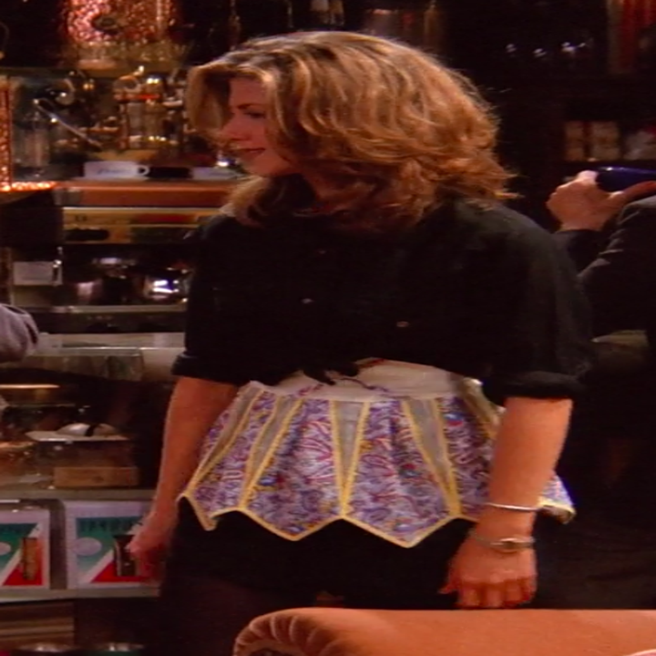 Rachel wearing tights, a miniskirt, an apron, and a long-sleeve button-up tied to be a crop top