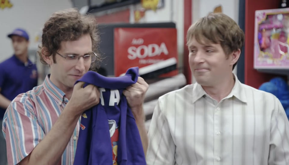 Kyle Mooney holds a Pogie Pepperoni's shirt, staring at it awe