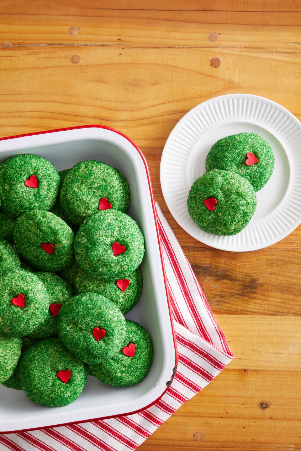 grinch cookies covered in green sugar with a red candy heart pressed into them