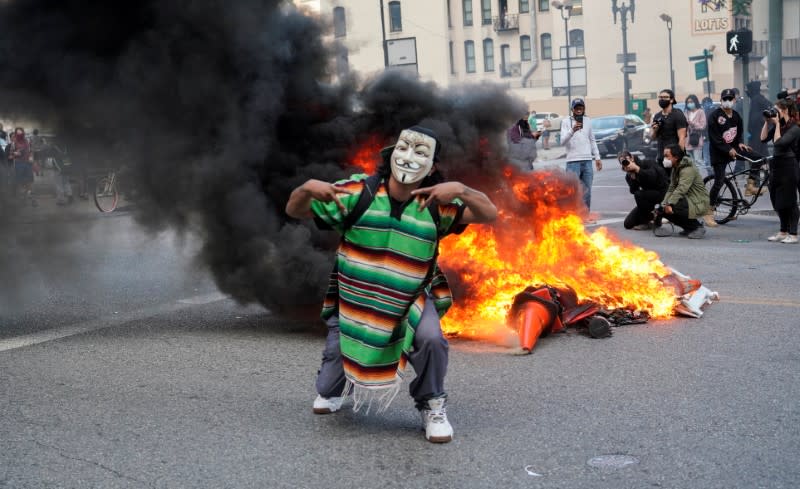 Un manifestante enmascarado se para frente al fuego, en Los Ángeles, California