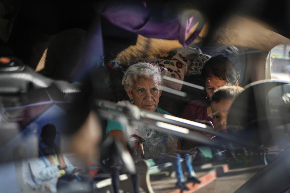 Reflected in the rear view mirror of a car, Venezuelan migrant Dominga de Cardozo waits to travel to the border with Brazil, in Santa Elena de Uairen, Venezuela, Wednesday, April 5, 2023. People of all ages are increasingly leaving their home country for the first time with their sights set on neighboring Brazil. (AP Photo/Matias Delacroix)