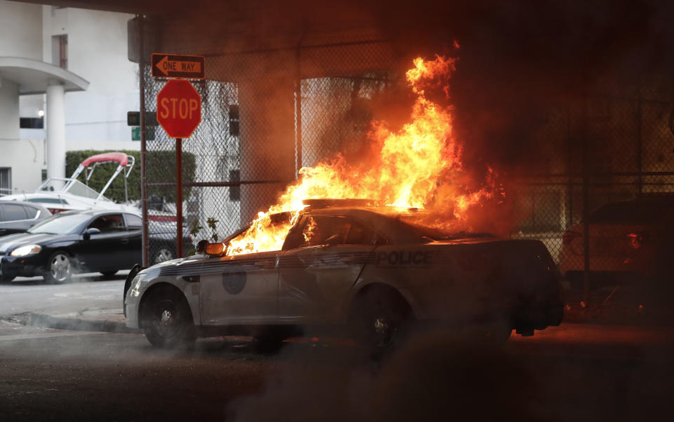 A police car burns during a demonstration next to the city of Miami Police Department, Saturday, May 30, 2020, downtown in Miami. Protests were held throughout the country over the death of George Floyd, a black man who died after being restrained by Minneapolis police officers on May 25.(AP Photo/Wilfredo Lee)