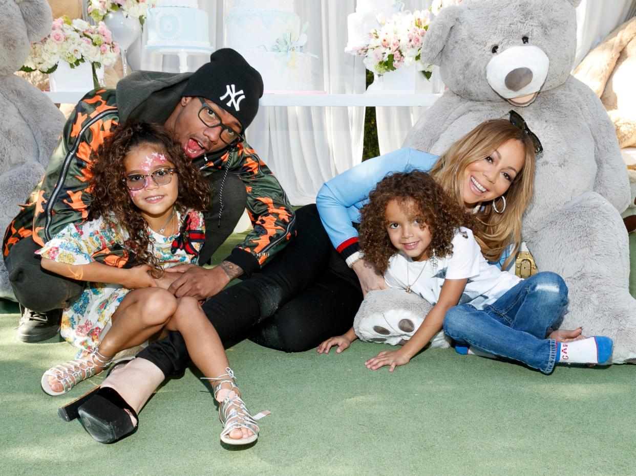 nick cannon holding daughter monroe cannon, and mariah carey holding son moroccan cannon, sitting on a green floor and smiling with large plush bears in the background