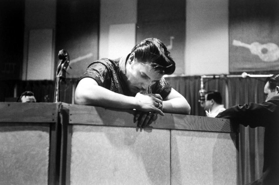 a black and white photo of elvis presley in a recording studio, resting his arms against a wall and looking down