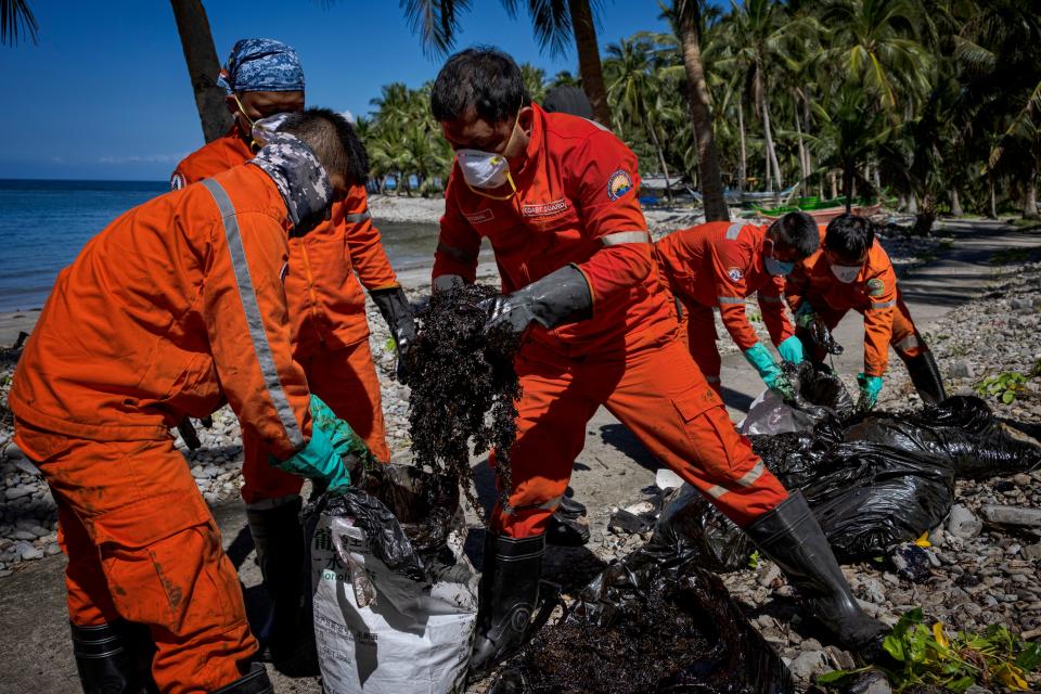 Coast guard personnel clean up an oil slick that has washed ashore from the sunken tanker MT Princess Empress.