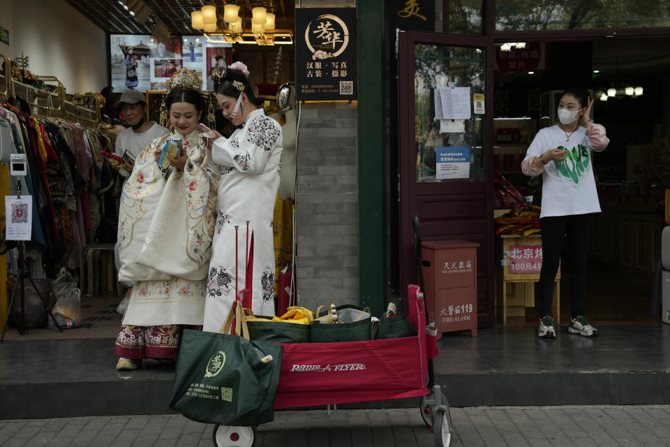 Women wearing traditional costumes wait outside a photography store catering to tourists in Beijing, Thursday, Sept. 29, 2022. A meeting of the ruling Communist Party to install leaders gives President Xi Jinping, China's most influential figure in decades, a chance to stack the ranks with allies who share his vision of intensifying pervasive control over entrepreneurs and technology development. (AP Photo/Ng Han Guan)