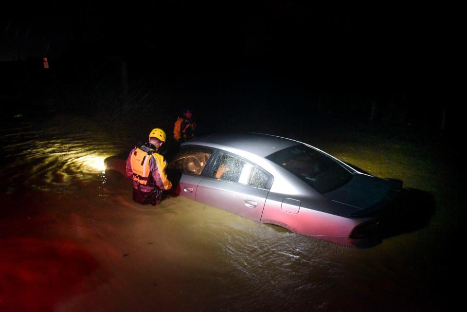 2 rescue people in helmets stand in waist-high water around a submerged car during Hurricane Irma