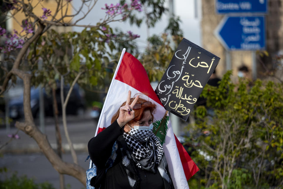 A protester holds a placard with Arabic that reads: "I yearn for my mother's freedom, my mother's justice and my mother's nation," as she participates in a march against the political leadership they blame for the economic, financial crisis and 4 Aug. Beirut blast, in Beirut, Lebanon, Saturday, March 20, 2021. (AP Photo/Hassan Ammar)