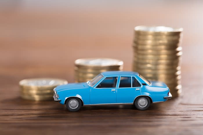 A miniature car in front of three stacks of coins.