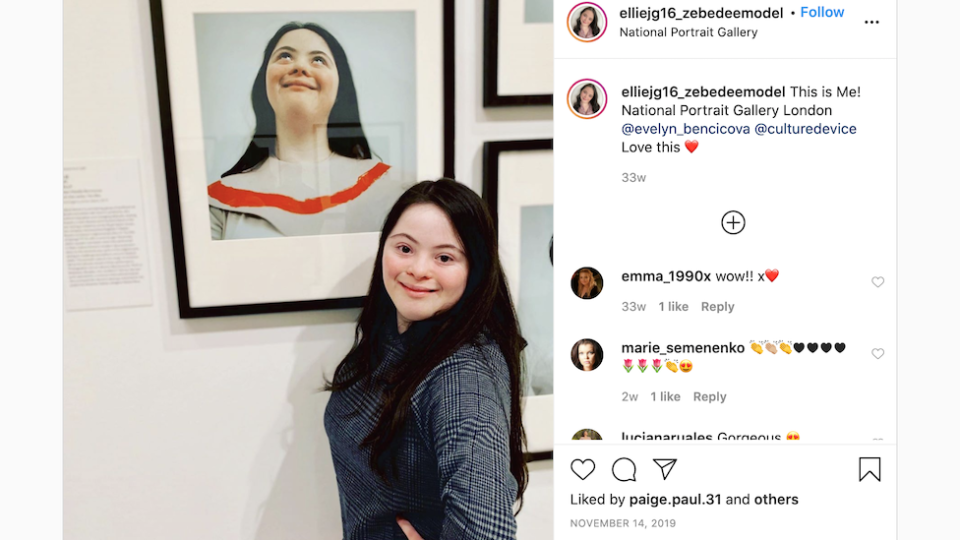 Ellie Goldstein posando junto a un retrato de ella misma expuesta en la National Portrait Gallery de Londres