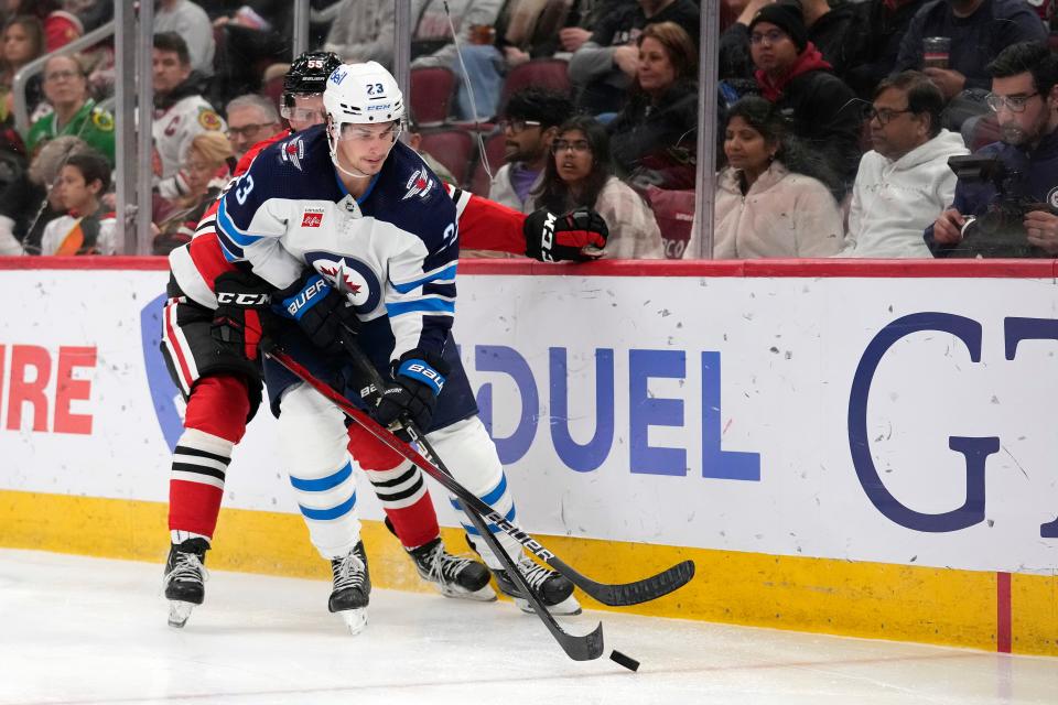 CHICAGO, ILLINOIS - FEBRUARY 23: Sean Monahan #23 of the Winnipeg Jets skates with the puck against Kevin Korchinski #55 of the Chicago Blackhawks during the third period at the United Center on February 23, 2024 in Chicago, Illinois. (Photo by Patrick McDermott/Getty Images)