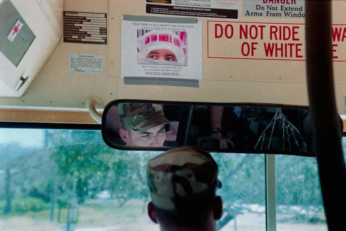 Ein Bus der US-Marine. Über dem Fahrer hängt ein Schild mit einem Foto einer Kopftuch tragenden Frau, auf dem steht: „Go to Hell USA“.