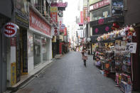 A woman wearing a face mask as a precaution against the coronavirus walks along a shopping street in Seoul, South Korea, Sunday, Nov. 29, 2020. South Korea is shutting down indoor gyms offering intense workout classes and banning year-end parties at hotels in the greater Seoul area to fight the virus. Prime Minister Chung Sye-kyun said Sunday.(AP Photo/Ahn Young-joon)