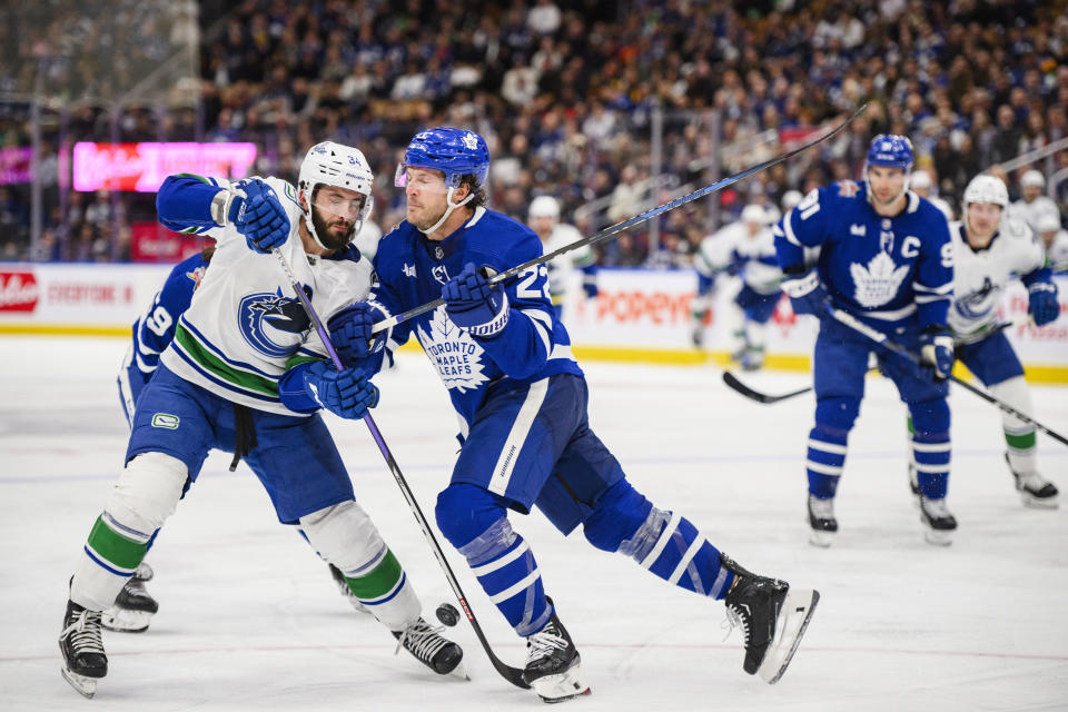 Toronto Maple Leafs defenseman Jake McCabe (22) checks Vancouver Canucks left wing Phillip Di Giuseppe (34) during the third period of an NHL hockey match in Toronto on Saturday, Nov. 11, 2023. (Christopher Katsarov/The Canadian Press via AP)