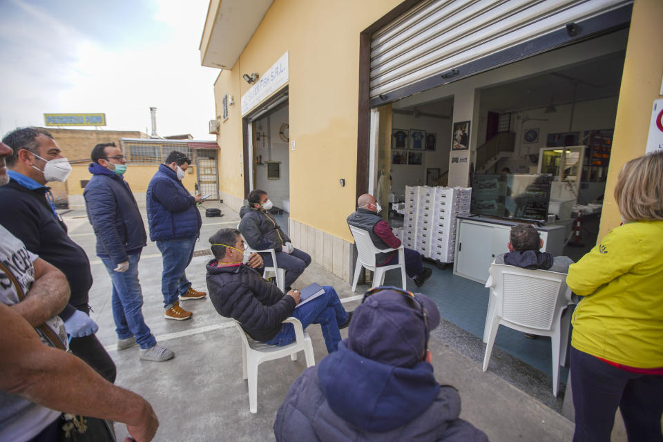 Buyers wear protective mask and respect safety distances as they attend an auction at the Silver Fish wholesale auction house, displayed on a television set in order to avoid overcrowding, in Fiumicino, Monday, March 30, 2020. Italy’s fishermen still go out to sea at night, but not as frequently in recent weeks since demand is down amid the country's devastating coronavirus outbreak. The new coronavirus causes mild or moderate symptoms for most people, but for some, especially older adults and people with existing health problems, it can cause more severe illness or death. (AP Photo/Andrew Medichini)