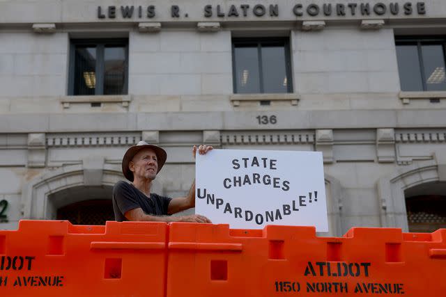 <p>Joe Raedle/Getty </p> An anti-Trump protester holds a sign next to the barricade set up in front of Fulton County Courthouse in August 2023