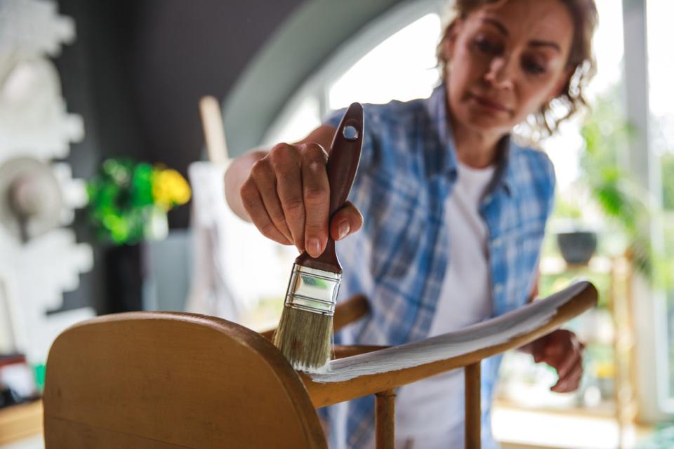 Mature woman painting a chair with white paint