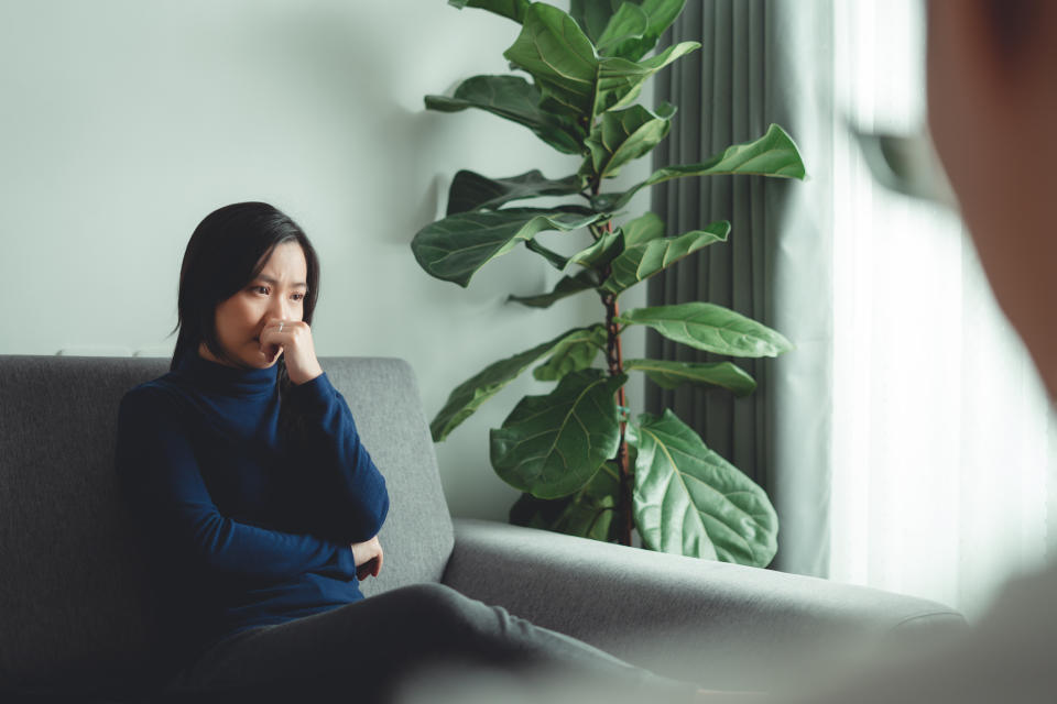 Person on a couch appears contemplative with a large plant beside them