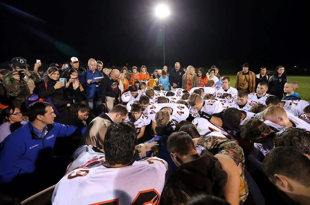El entrenador asistente de fútbol americano, Joseph Kennedy, rodeado de jugadores mientras se arrodillan para rezar con él en la cancha durante un juego en 2015 (AP)