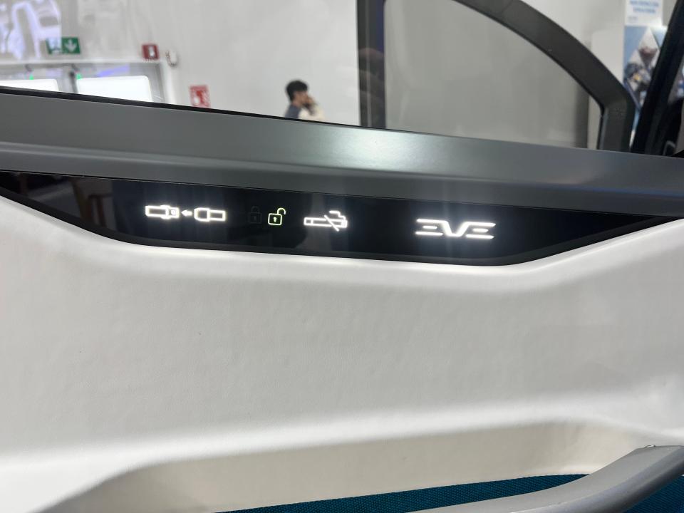 Seatbelt and no-smoking signs next to the Eve Air Mobility logo in LED lights on the door of a cabin model.