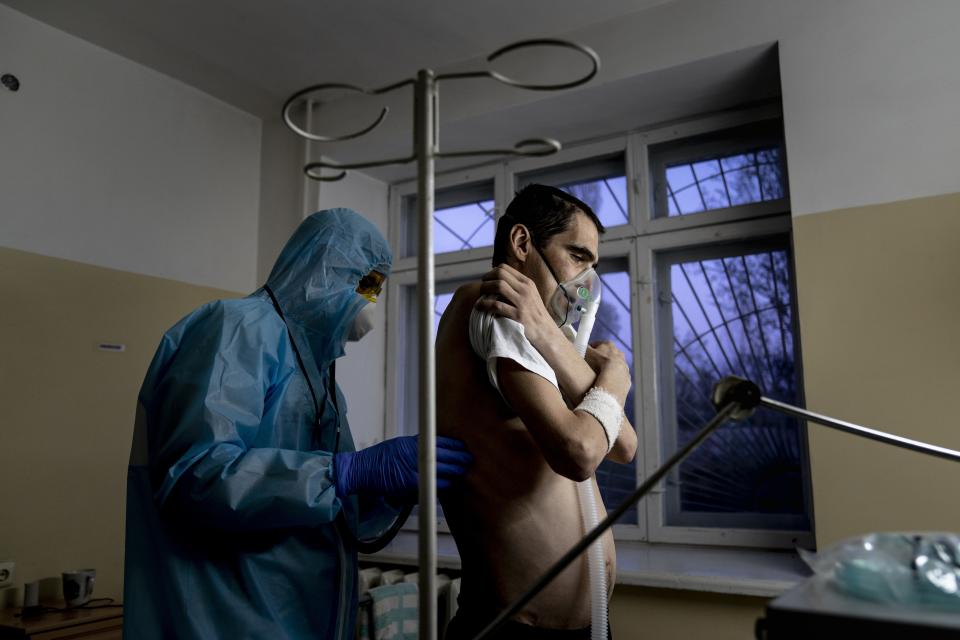 In this photo taken on Tuesday, April 28, 2020, a doctor, wearing a special suit to protect against coronavirus, checks a patient with coronavirus with a stethoscope during evening examination at a hospital in Malyn, Ukraine. Ukraine's troubled health care system has been overwhelmed by COVID-19, even though it has reported a relatively low number of cases. (AP Photo/Evgeniy Maloletka)