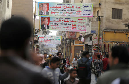 People walk under posters of Egyptian President Abdel Fattah al-Sisi for the upcoming presidential election on Al-Mo'ez street, in Cairo, Egypt March 19, 2018. REUTERS/Mohamed Abd El Ghany