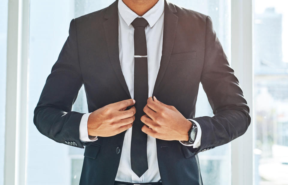 Professional in a suit adjusting tie, representing business attire for Work & Money article