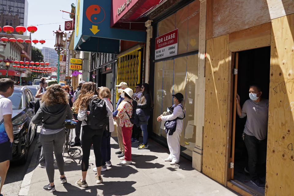 A worker in a Chinatown storefront under renovation looks out at a tour group on Grant Avenue in San Francisco, Monday, May 23, 2022. Chinatowns and other Asian American enclaves across the U.S. are using art and culture to show they are safe and vibrant hubs nearly three years after the start of the pandemic. (AP Photo/Eric Risberg)