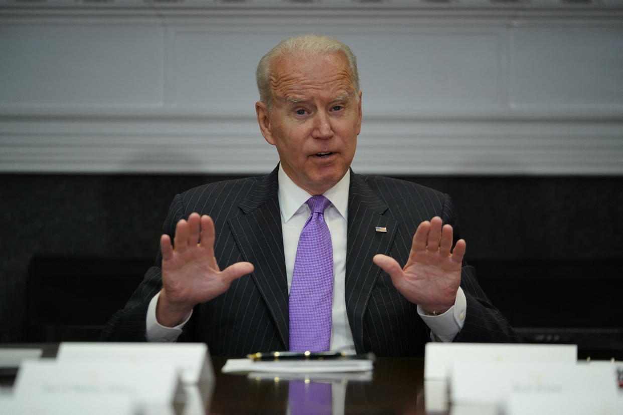 President Biden, seated at a table, gestures with both hands extended in front of him