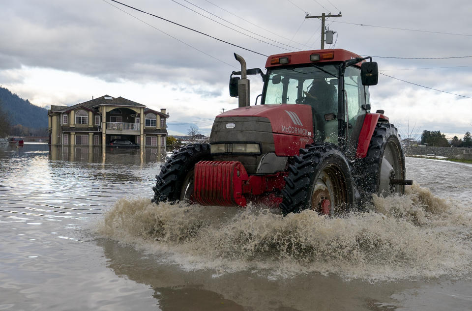 A tractor drives over a flooded road following heavy rain and mudslides in Abbotsford, British Columbia, Friday, Nov. 19, 2021. (Jonathan Hayward/The Canadian Press via AP)