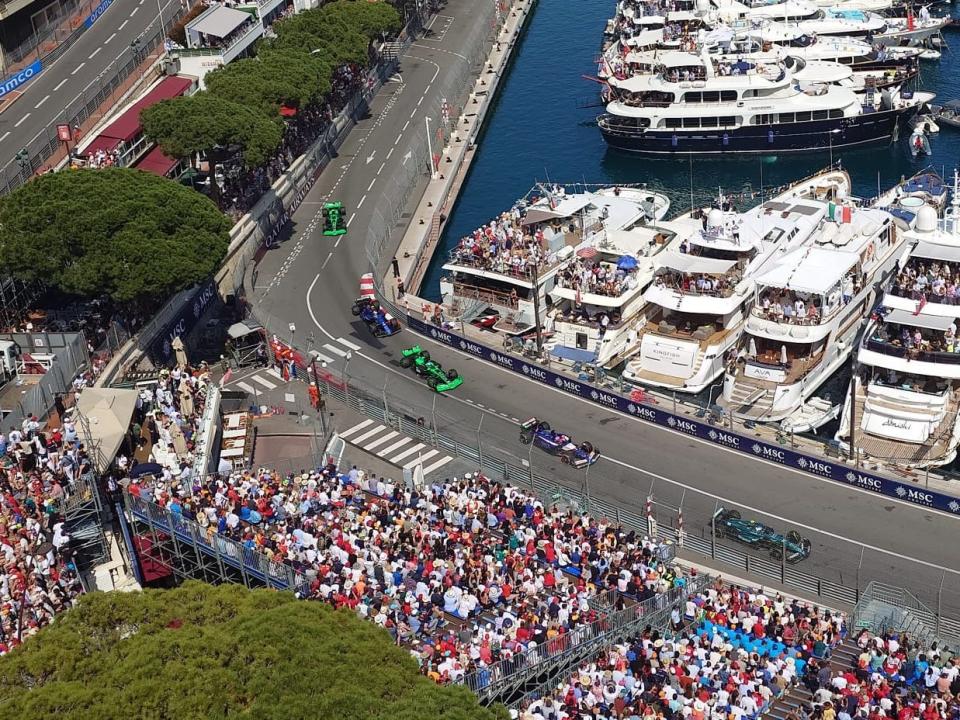 Racecars on Grand Prix race track, with thousands of people in stands and on yachts in the French Riviera, which is next to the race track