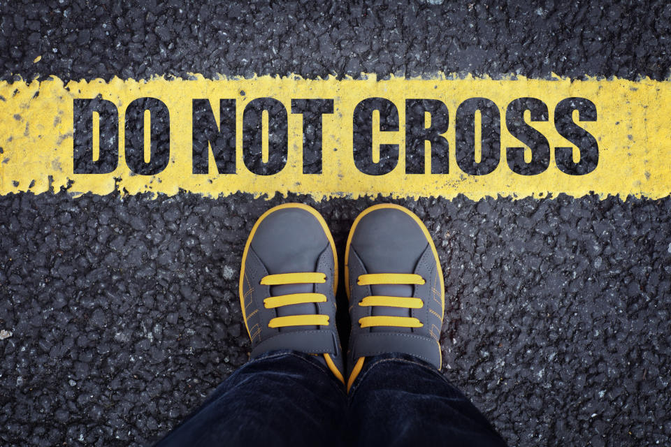 A person stands in front of a line that reads "Do not cross"
