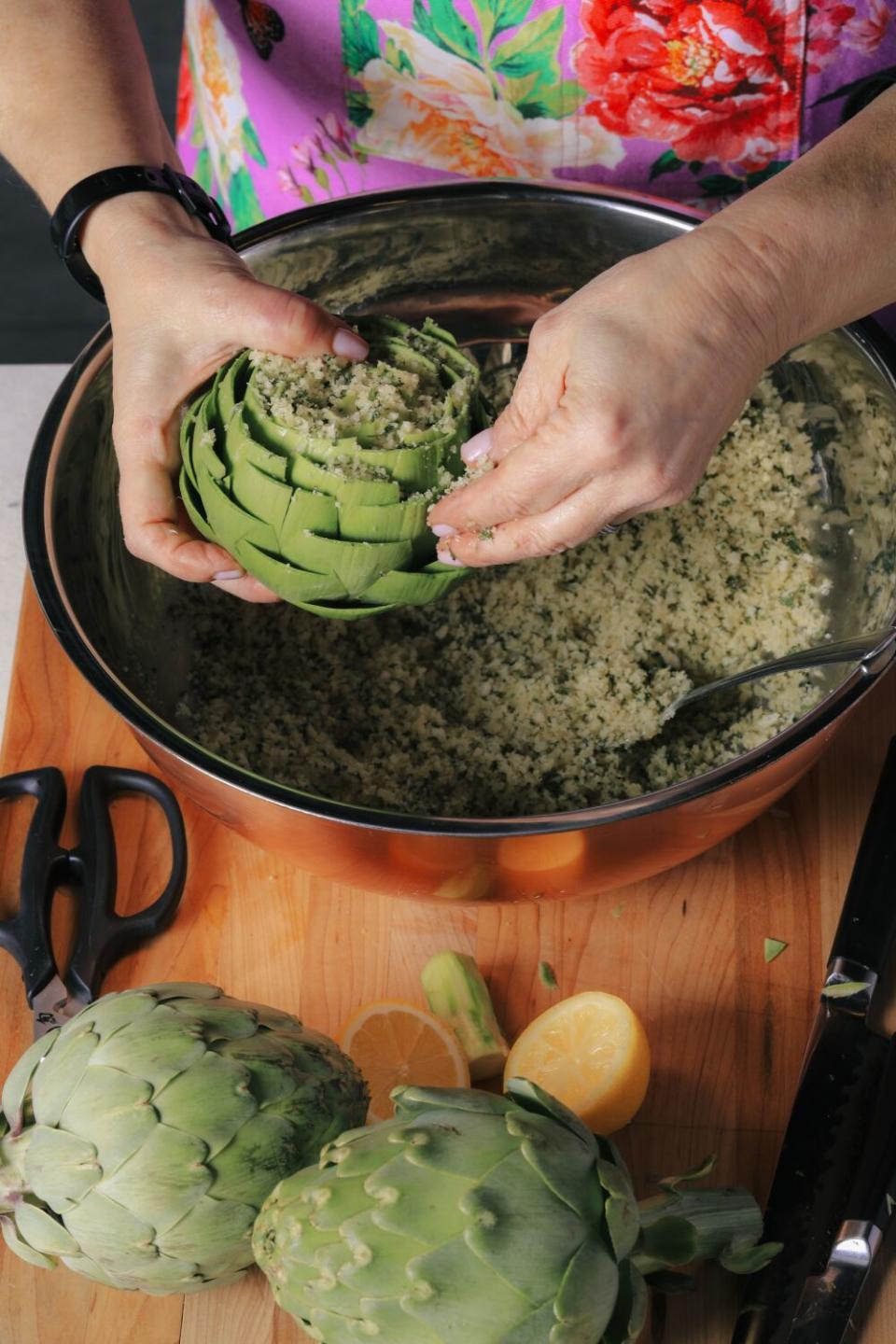 Hands holding an artichoke over a pan of stuffing
