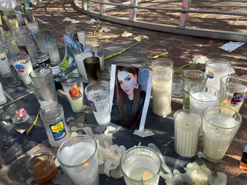 A portrait of a woman with long dark hair sits on the ground, surrounded by candles