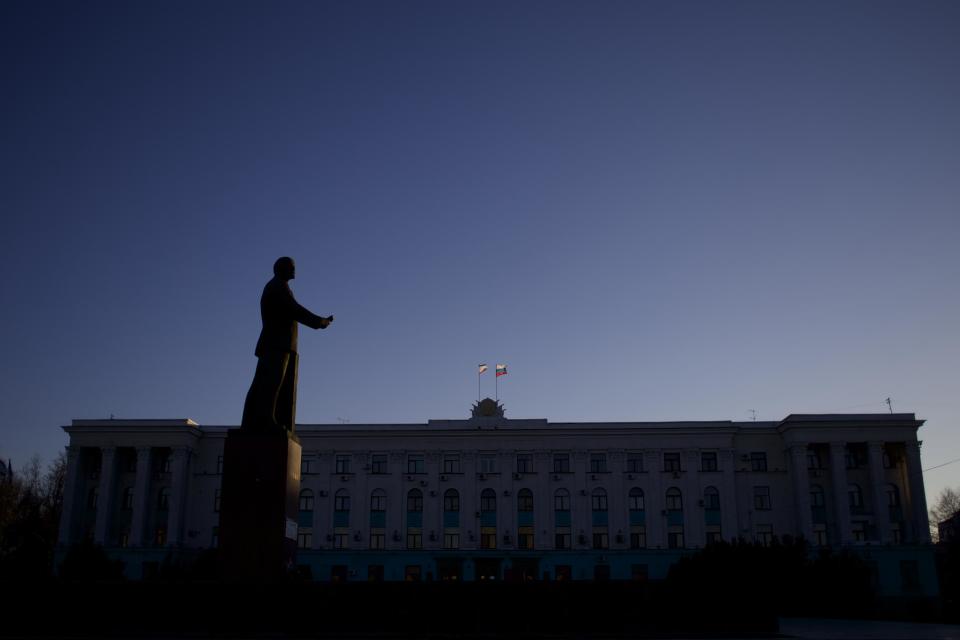 FILE - In this Saturday, March 15, 2014 file photo, the Russian and Crimean flags fly on a local government building as a statue of Soviet revolutionary leader and founder Vladimir Lenin is silhouetted by the setting sun in Simferopol, Ukraine. Despite the pebble beaches and cliff-hung castles that made Crimea famous as a Soviet resort hub, the Black Sea peninsula has long been a corruption-riddled backwater in economic terms. The Kremlin, which decided to take the region from Ukraine after its residents voted in a referendum to join Russia, has begun calculating exactly what it will cost to support Crimea’s shambolic economy _ which one Russian minister described as “no better than Palestine.” (AP Photo/Ivan Sekretarev, File)