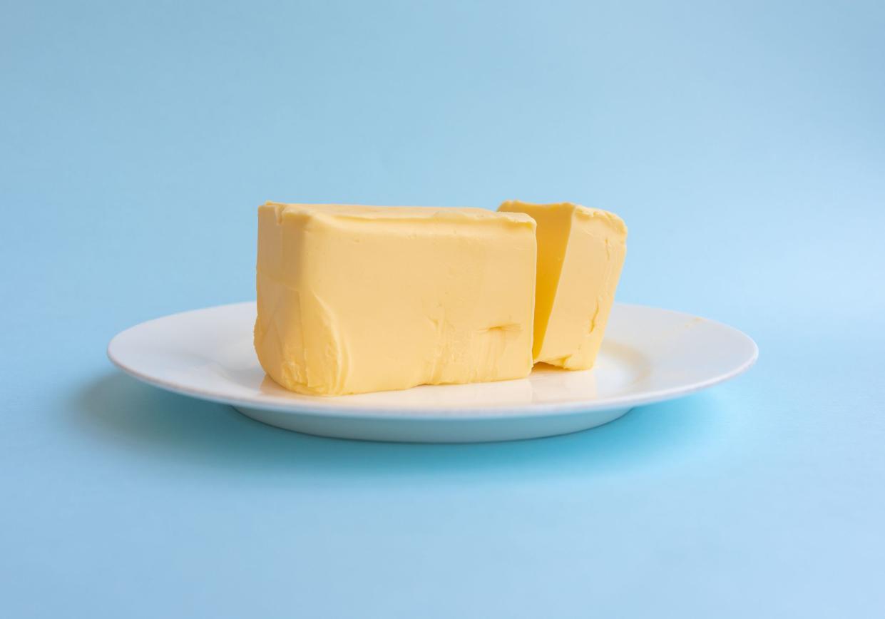 Bar of butter on a white plate, a piece is cut, with a light blue background